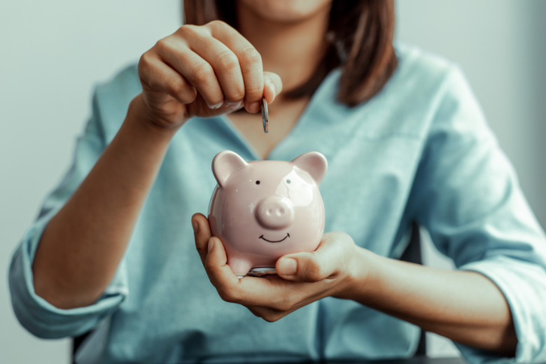 how to be financially free: a woman dropping a coin into a small pink piggy-bank