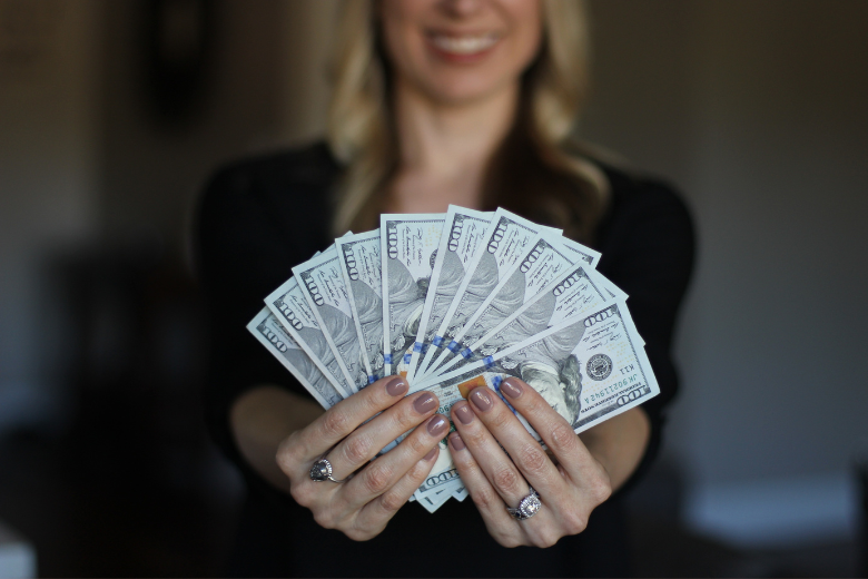 how to be financially free: a woman smiling confidently and fanning out several hundred dollar bills