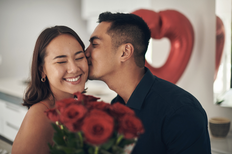 girlfriend and boyfriend kissing and holding a red bouquet of flowers