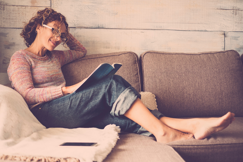 woman sitting on couch, smiling while reading a book 