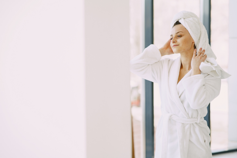 woman reading a white robe, smiling and touching head towel 