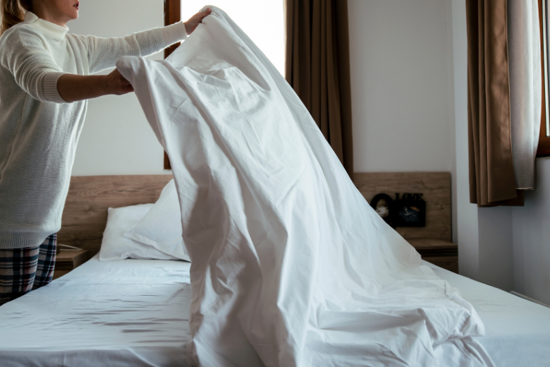 woman-holding-white-sheet-above-bed