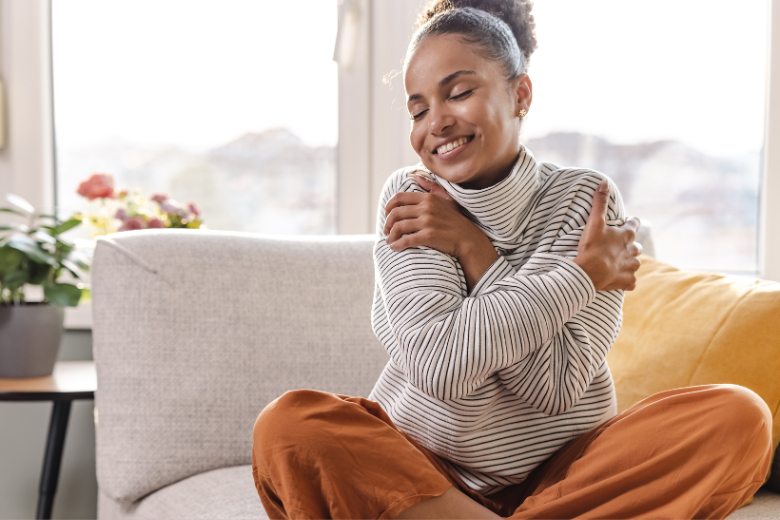 young-woman-sitting-on-sofa-hugging-herself